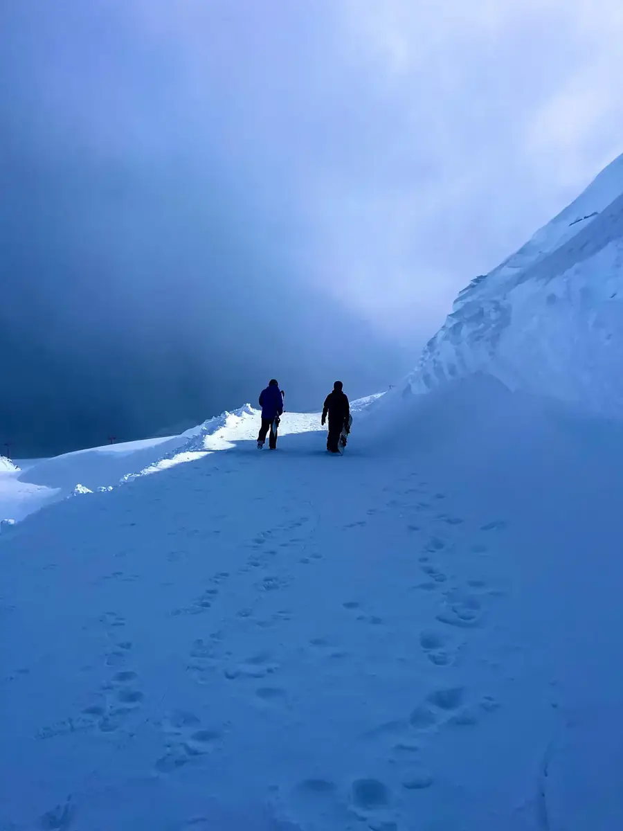 Duas pessoas caminhando na neve com pranchas de snowboard