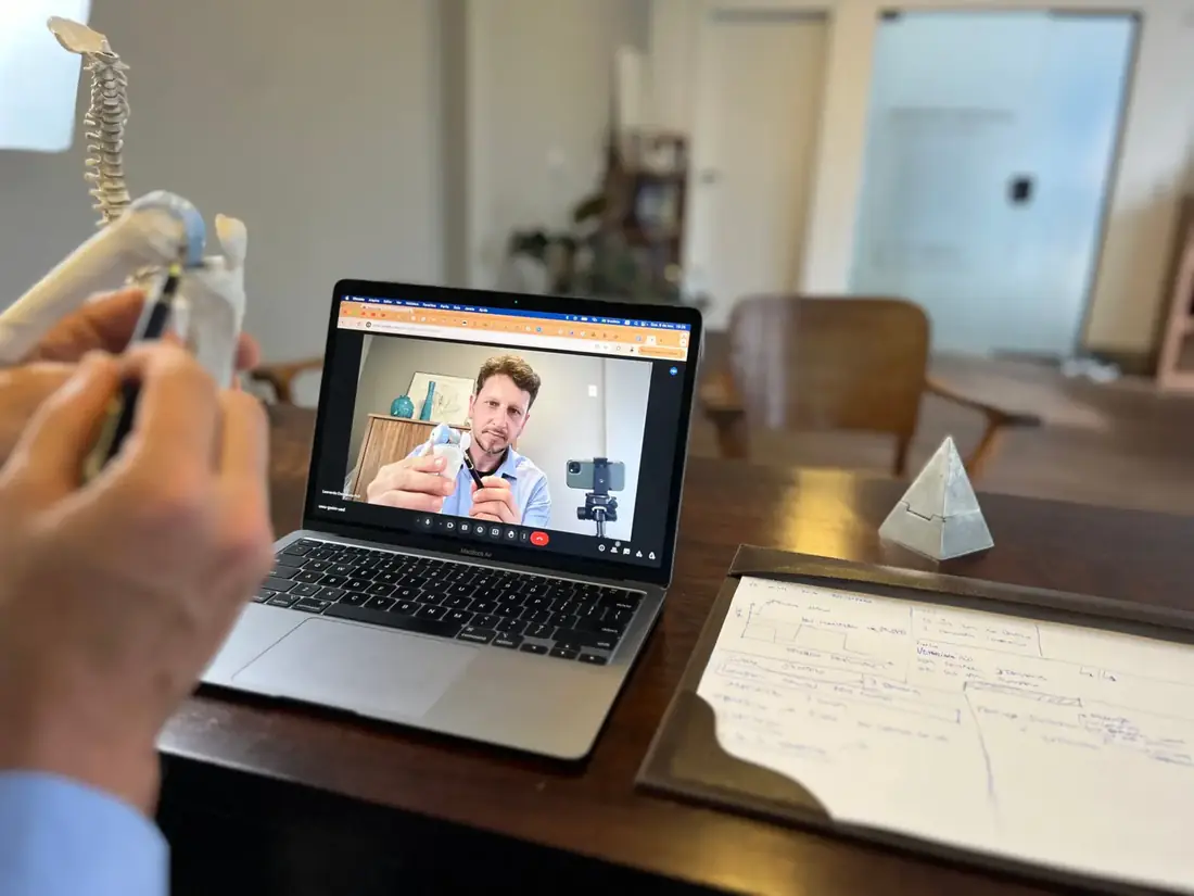 Consulta online: notebook aberto sobre a mesa do consultório, com o modelo de coluna e anotações